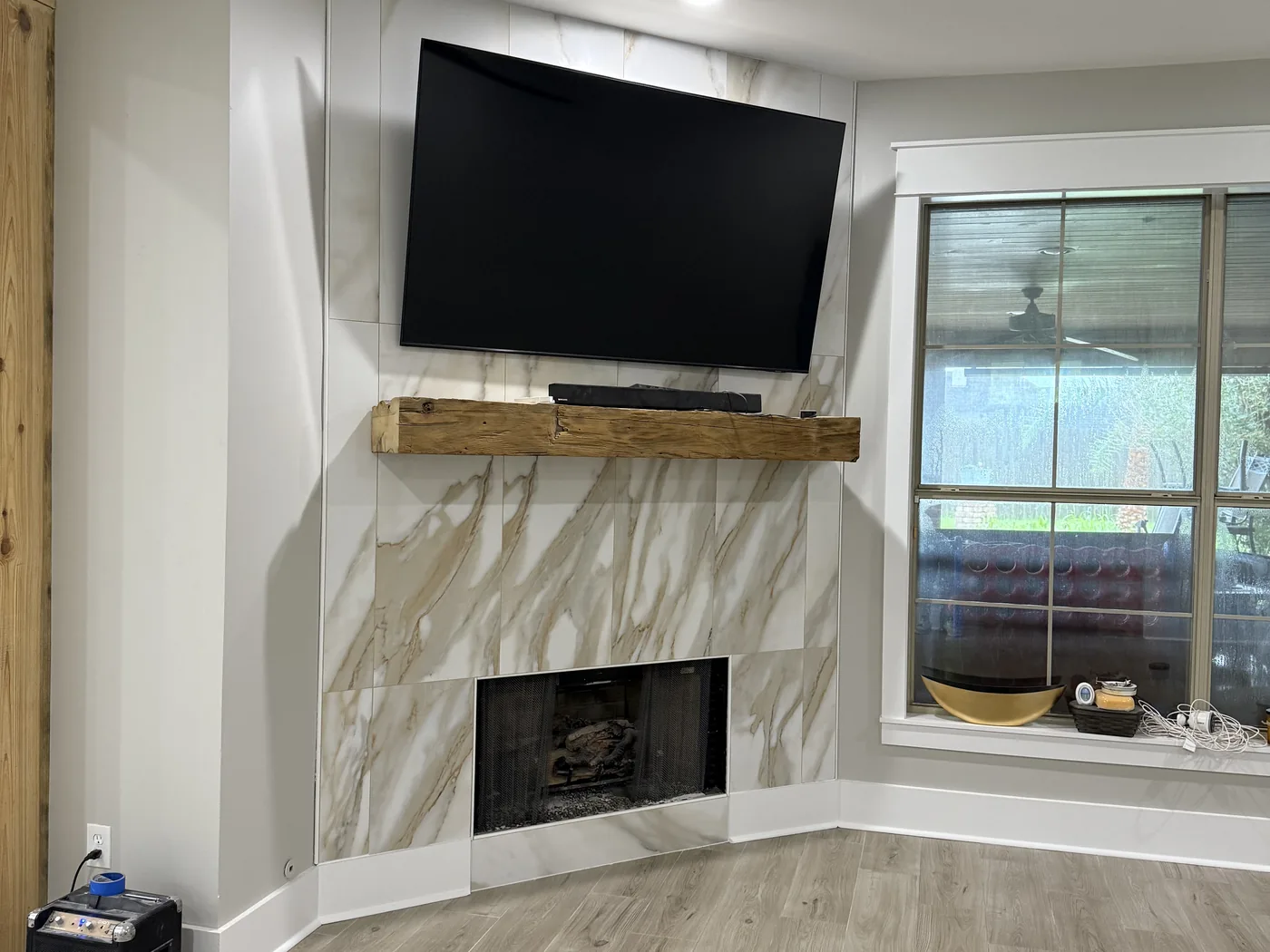 Light wood-look plank tile floor in a living room with a marble-veined tile fireplace surround and reclaimed beam mantel