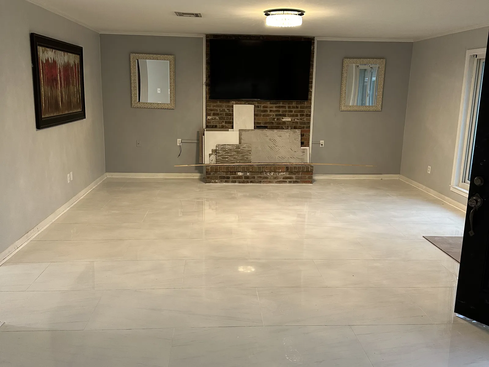 Large-format porcelain tile floor laid flat and even across a living room, with a brick fireplace wall in the background