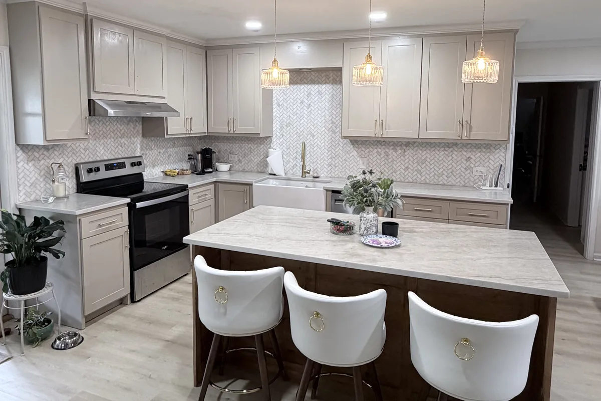 Remodeled kitchen with taupe shaker cabinets, herringbone backsplash, brass pulls and a stained wood island