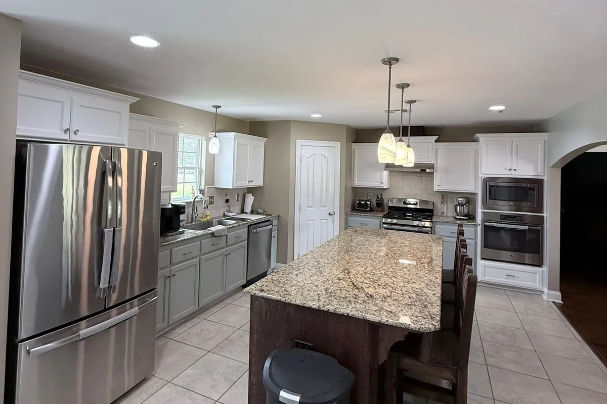 Kitchen with cabinets repainted white and sage green around a dark island