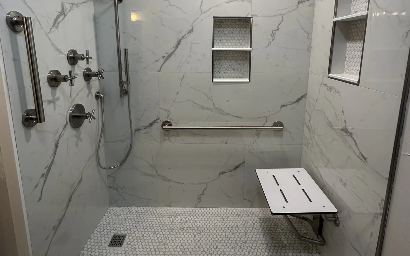 Large-format marble-look tile shower with double recessed niche, rain shower head and mosaic floor