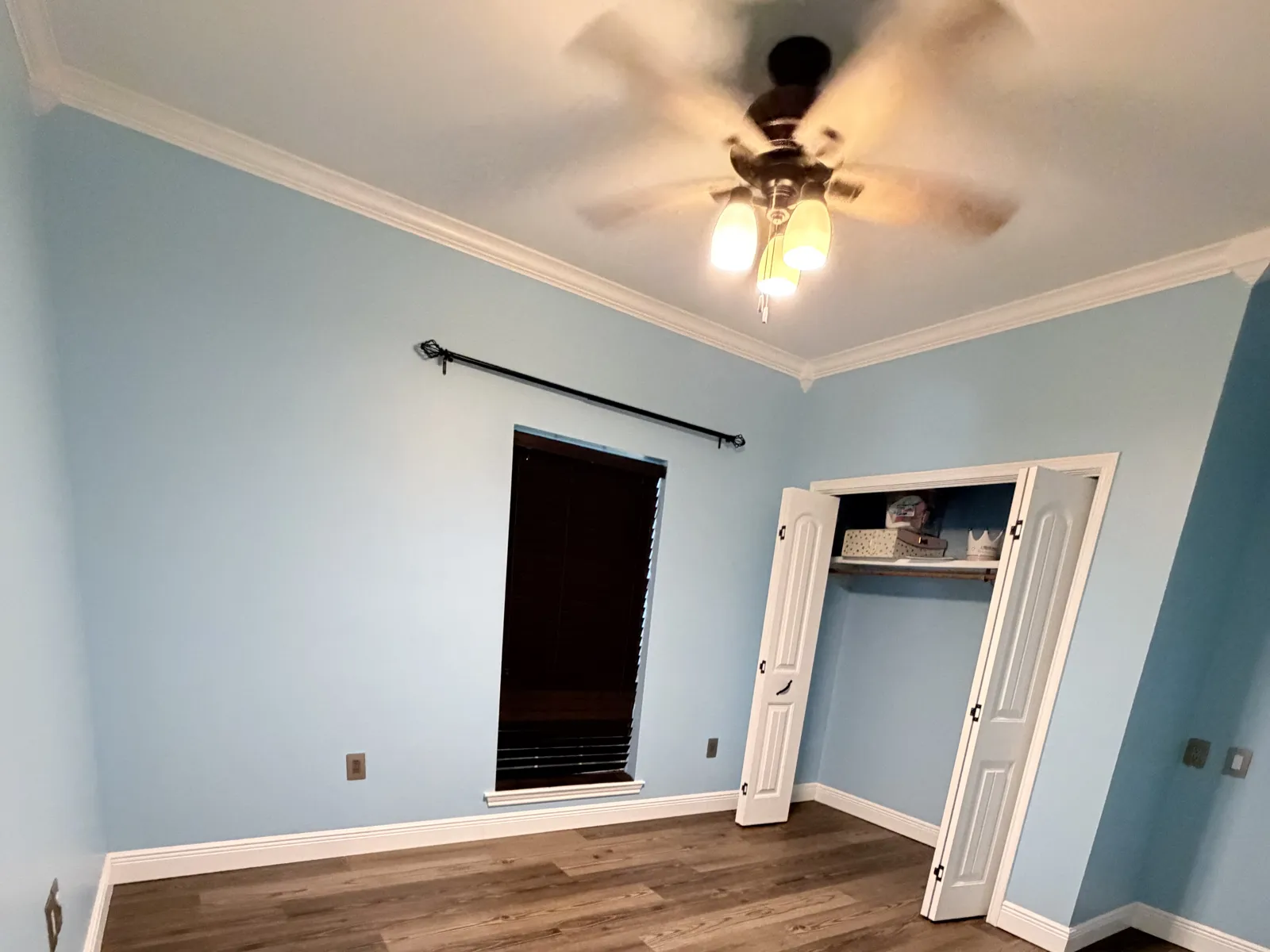 Freshly painted bedroom with light blue walls, white crown molding, baseboards and closet doors