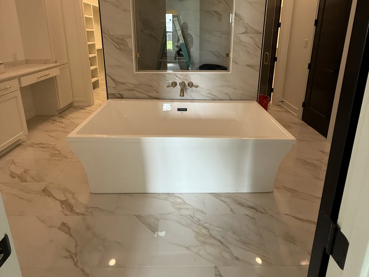 Primary bathroom with a freestanding tub, marble-look floor tile and a tiled feature wall