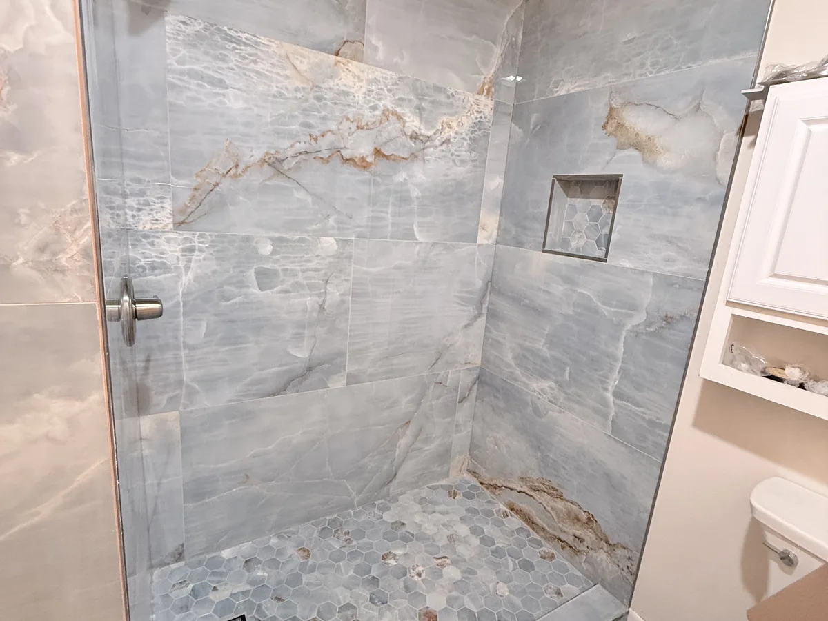 Finished walk-in shower with blue onyx-look wall tile, hex mosaic floor and a recessed niche