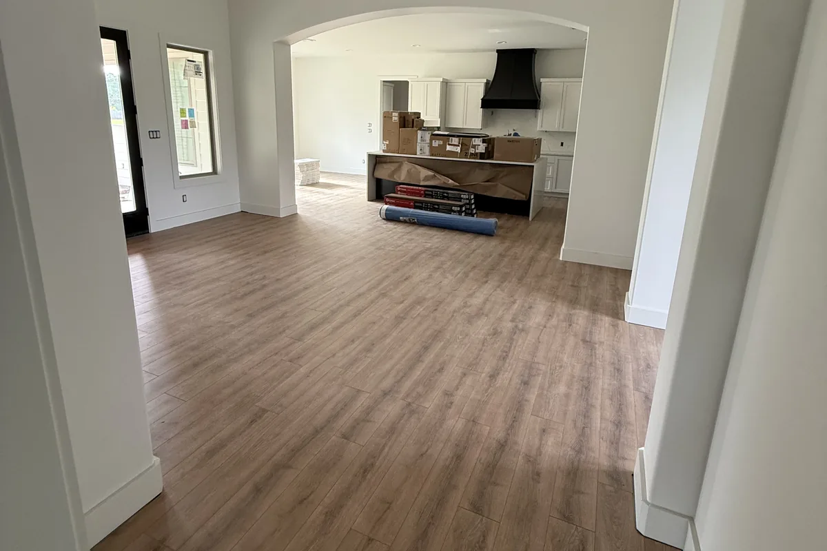 Open living space with new plank flooring flowing through arched openings toward the kitchen
