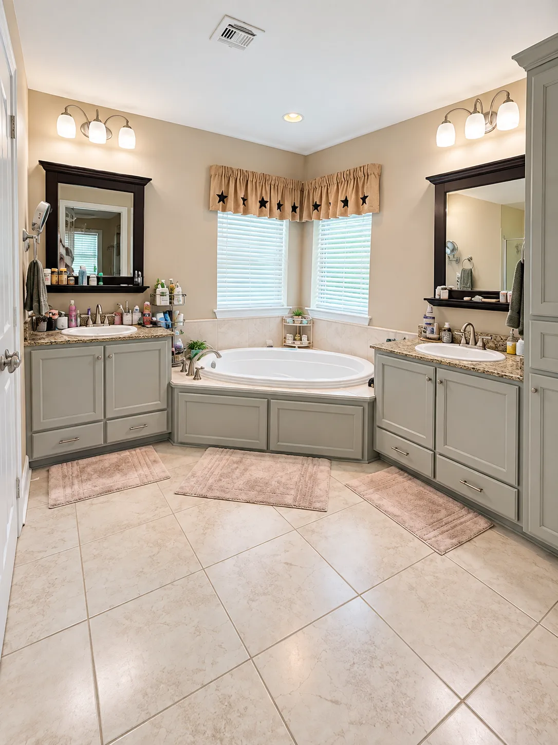 Primary bathroom with a corner soaking tub, double vanities with gray cabinets, and a large-format tile floor