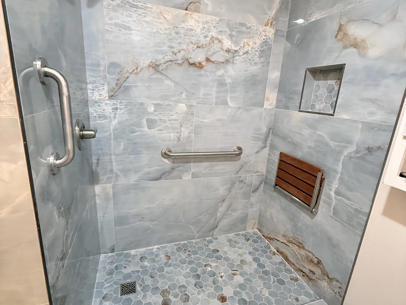 Walk-in shower tiled in blue onyx-look slabs with a hex mosaic floor, recessed niche and teak fold-down seat